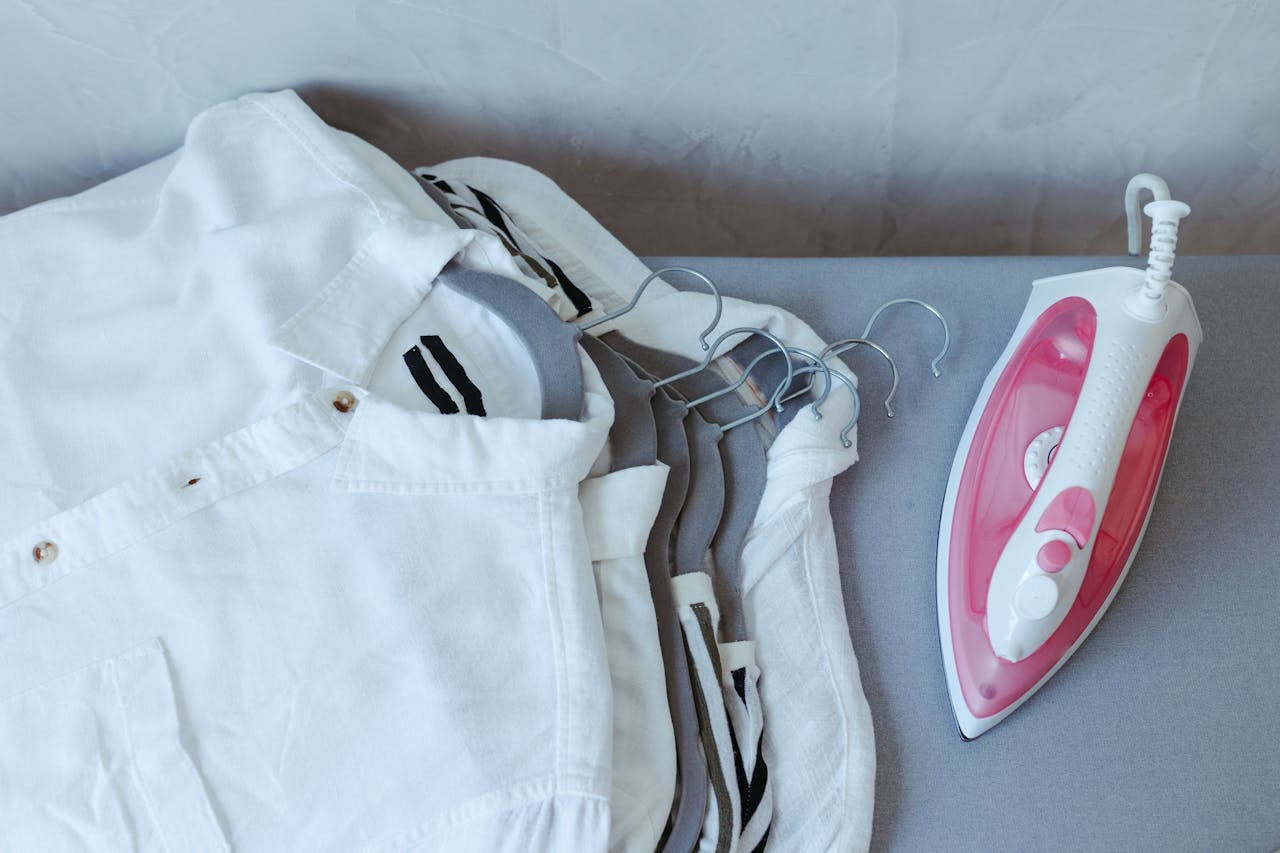 A flat lay of folded white shirts with a pink iron, illustrating sleek home care.