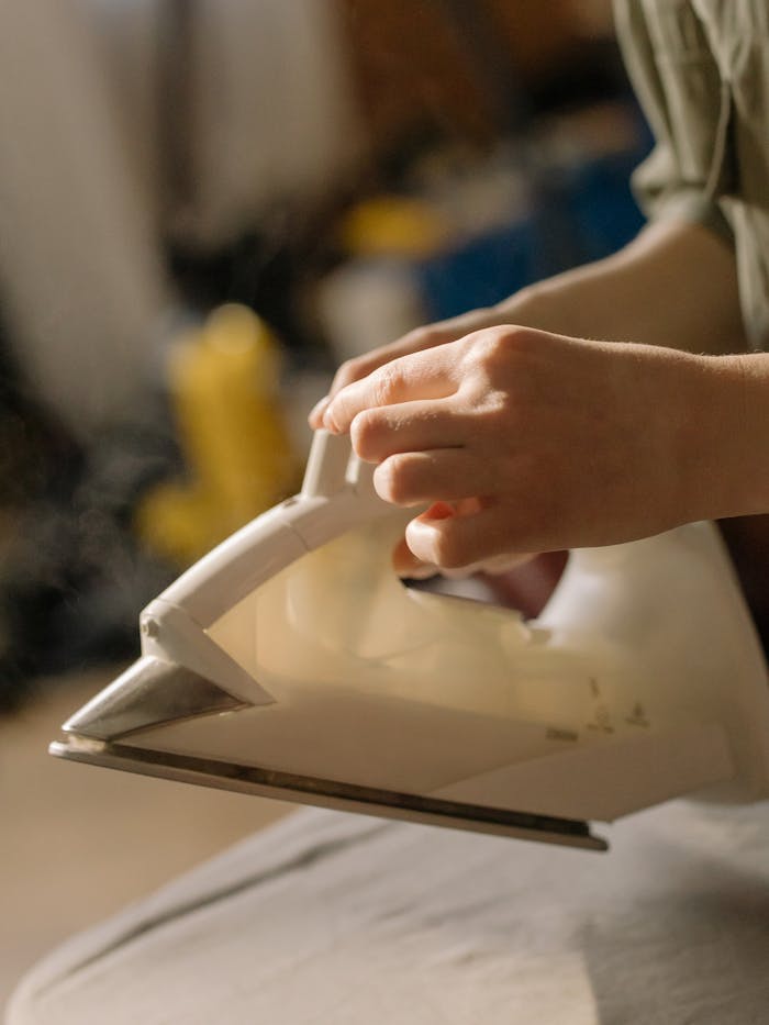 A person using a steam iron for household chores, set against a cozy home backdrop.