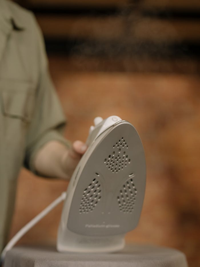 A close-up image captures a hand holding a steam iron indoors, showcasing home care.