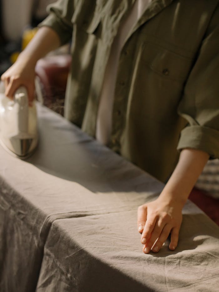 A person ironing clothes on a board in a cozy home setting, focusing on hands and technique.