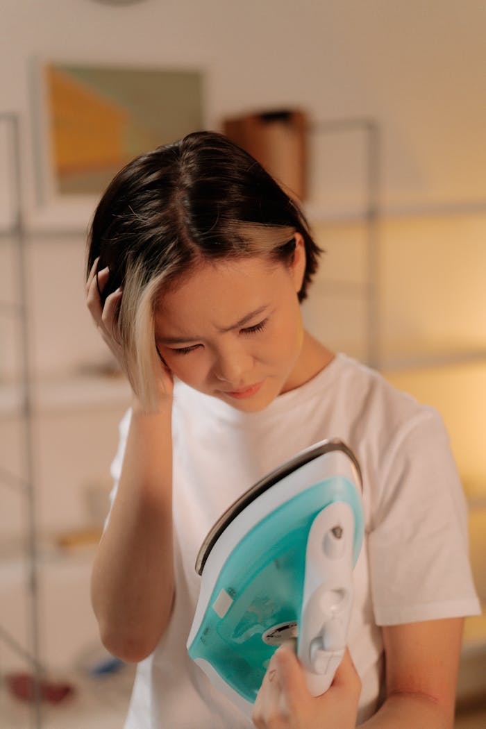 A young woman looks upset while holding an iron, indicating a mishap during ironing.